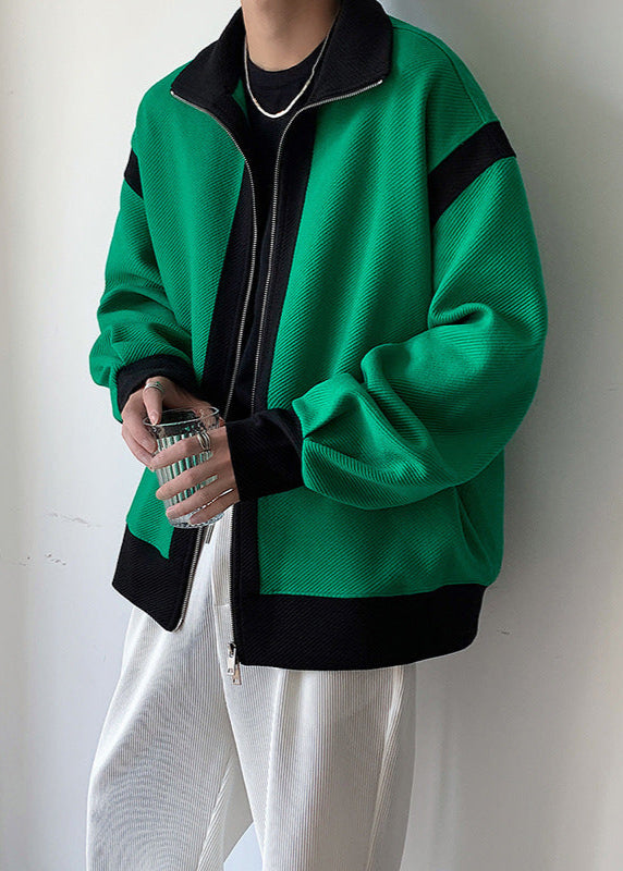 Giacca verde con dettagli neri, zip frontale, indossata da una persona. Moda casual, stile urbano, abbinata a pantaloni bianchi.
