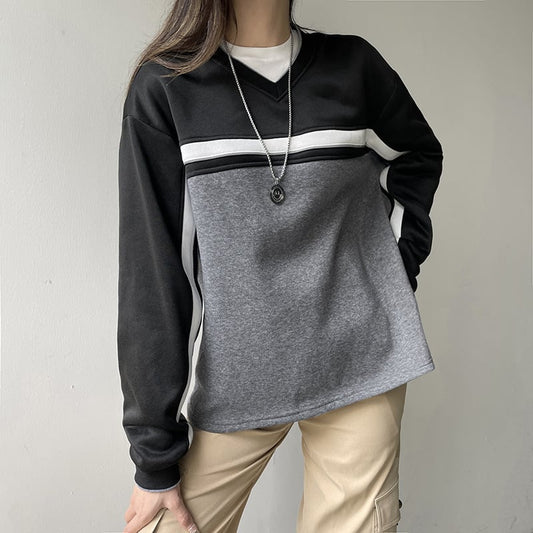 Donna con maglia a maniche lunghe nera e grigia, pantaloni beige, collana argento. Moda casual autunnale, abbigliamento streetwear femminile.