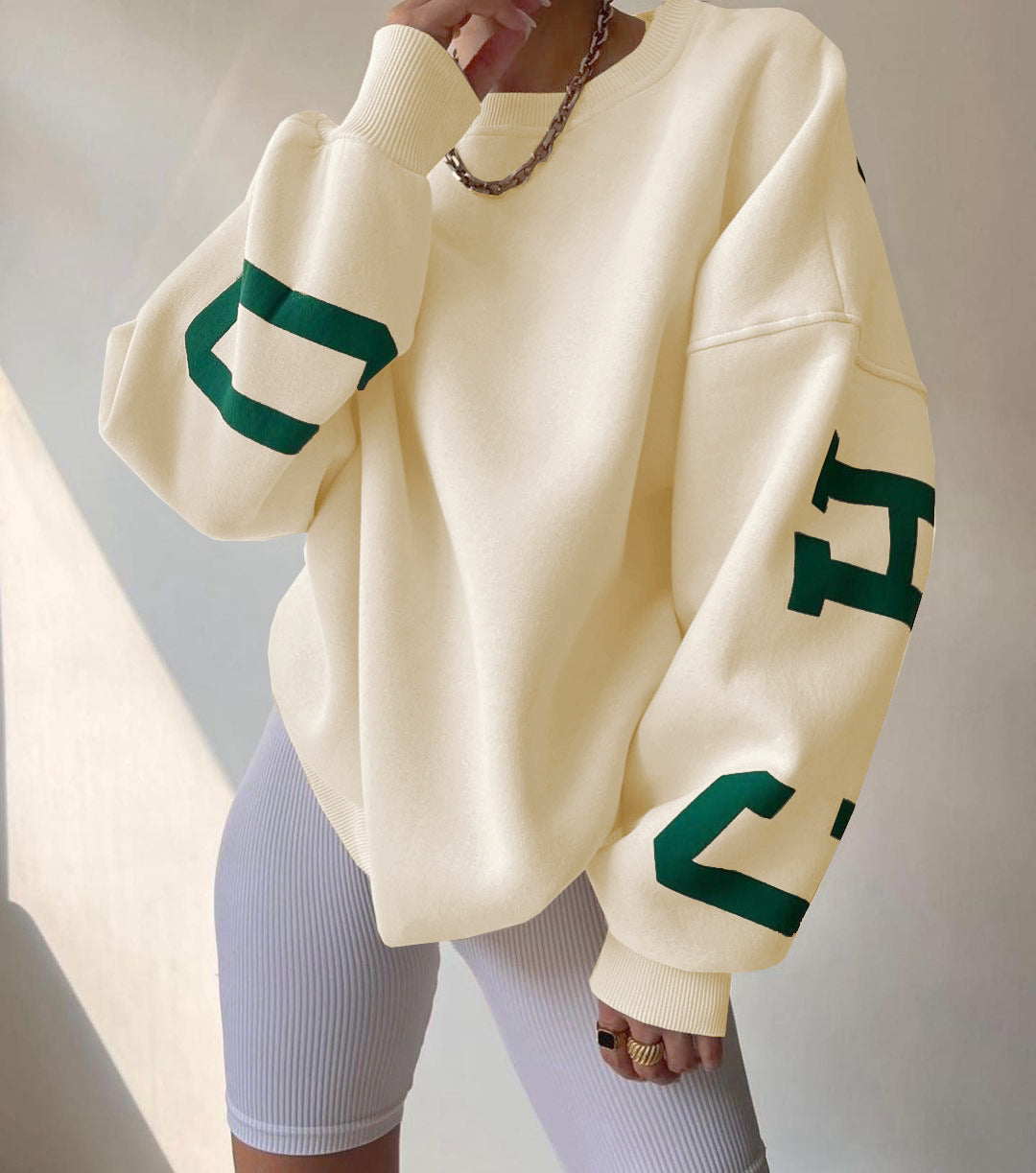 Felpa oversize beige con lettere verdi, abbinata a pantaloncini bianchi a coste. Stile casual, moda streetwear, tendenza abbigliamento 2023.