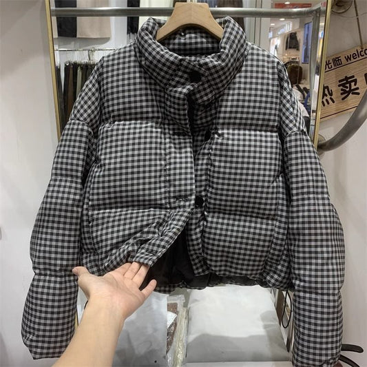 Giacca imbottita a quadri bianchi e neri, appesa su gruccia in negozio. Moda invernale, abbigliamento caldo, stile casual.