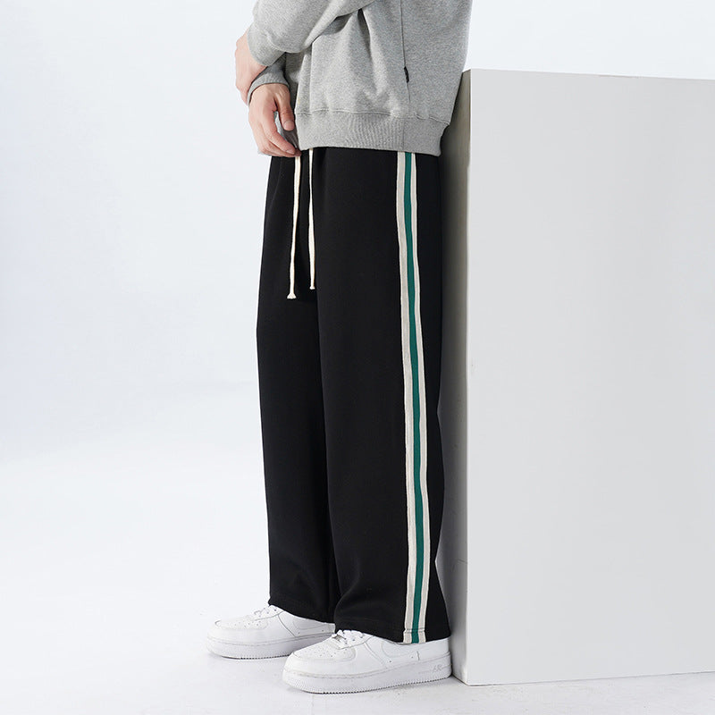 Pantaloni sportivi neri con strisce laterali verdi e bianche, indossati con felpa grigia e scarpe bianche. Moda casual uomo, abbigliamento comodo.