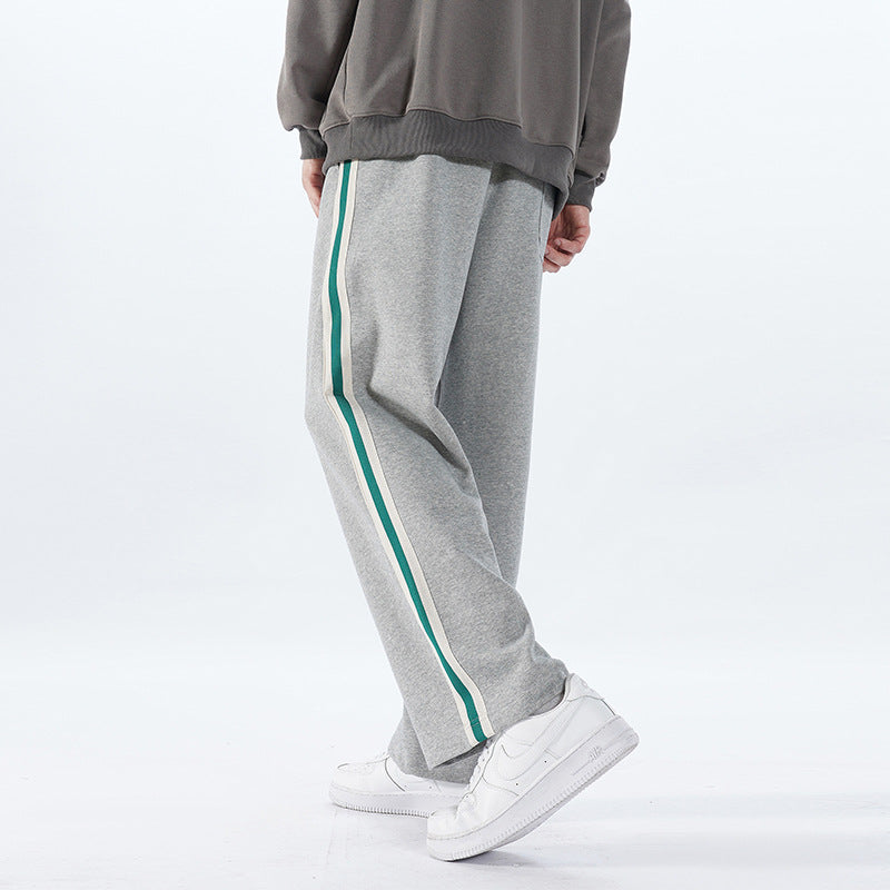 Pantaloni sportivi grigi con striscia verde, indossati con scarpe da ginnastica bianche. Moda casual uomo, abbigliamento comodo e trendy.