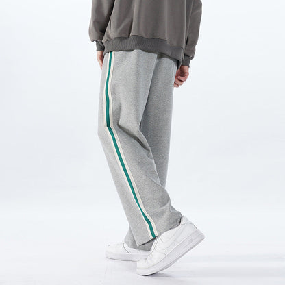 Pantaloni sportivi grigi con striscia verde, indossati con scarpe da ginnastica bianche. Moda casual uomo, abbigliamento comodo e trendy.