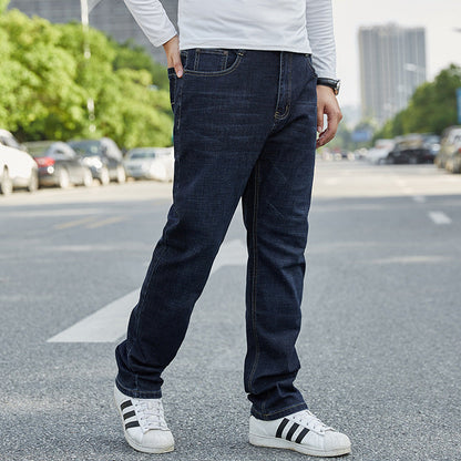 Uomo in jeans blu scuro e scarpe da ginnastica bianche su strada cittadina, sfondo urbano con alberi e auto parcheggiate.
