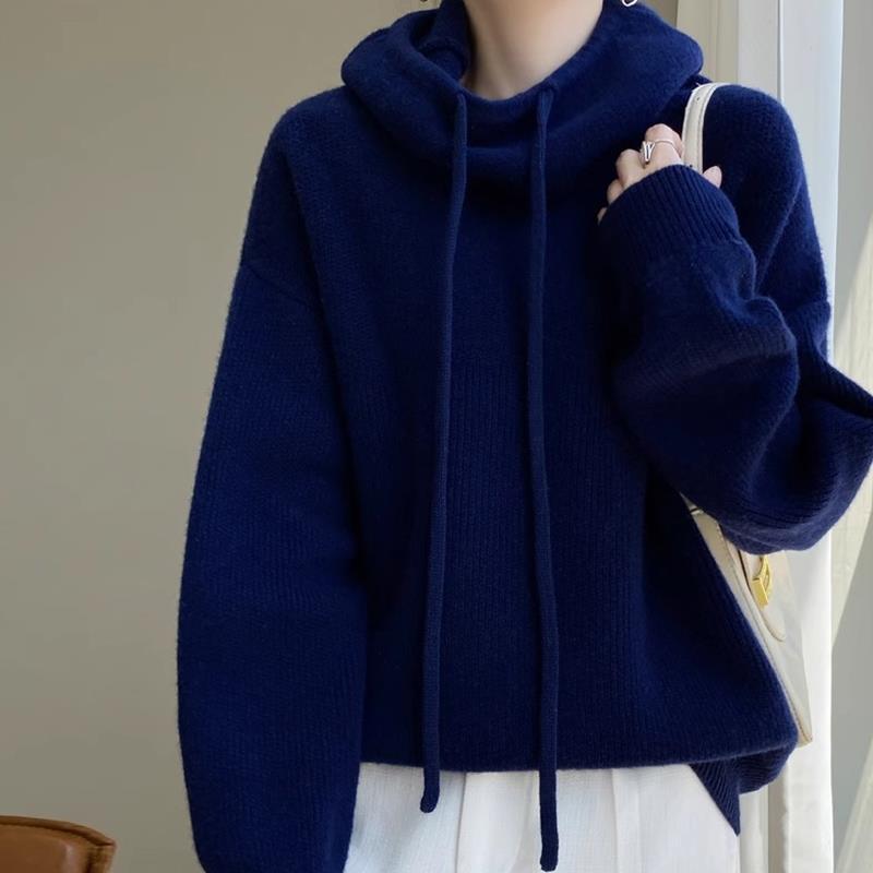 Maglione blu scuro con cappuccio e lacci, indossato da una persona. Design casual e moderno, perfetto per l'autunno e l'inverno.