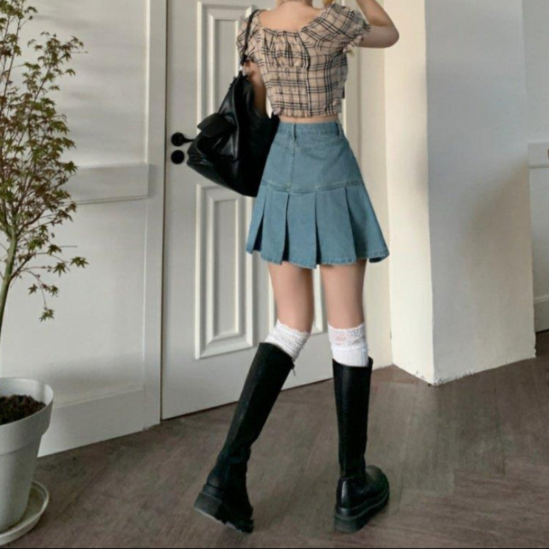 Giovane donna in minigonna di jeans e stivali neri, top a quadri, calze bianche, borsa nera, davanti a porta bianca. Moda casual femminile.