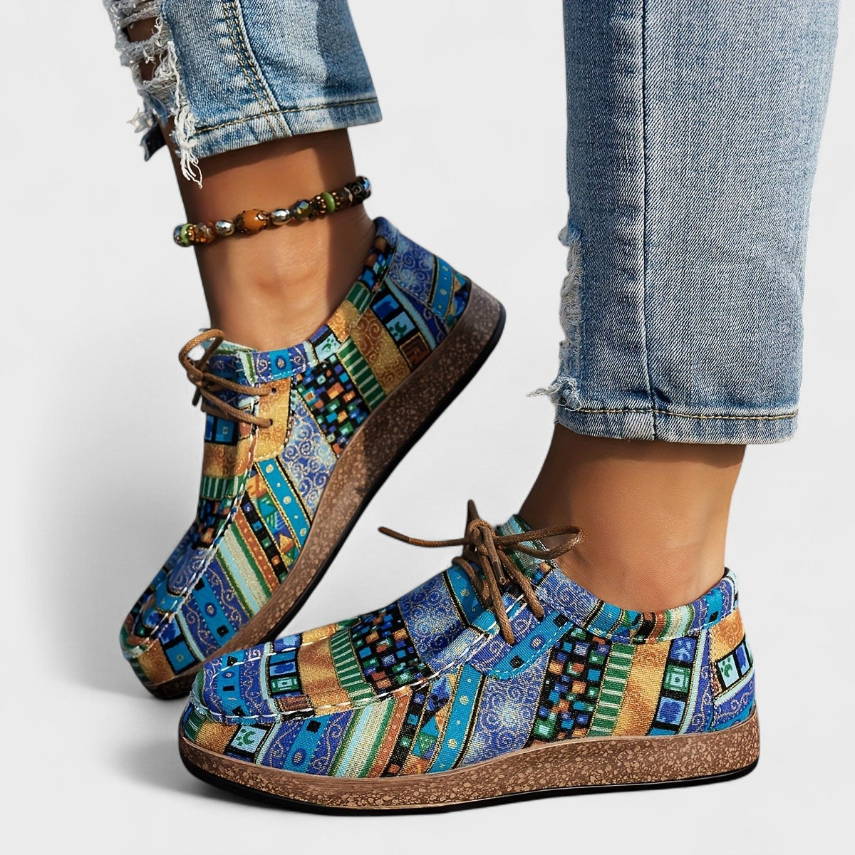 Scarpe colorate con motivo geometrico blu e verde, indossate con jeans strappati e cavigliera. Moda casual, calzature artistiche, stile boho.