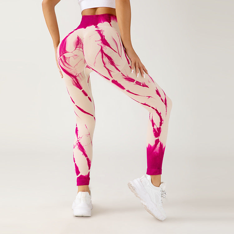 Donna in leggings sportivi tie-dye rosa e bianchi, scarpe da ginnastica bianche, posa su sfondo neutro. Abbigliamento fitness alla moda.
