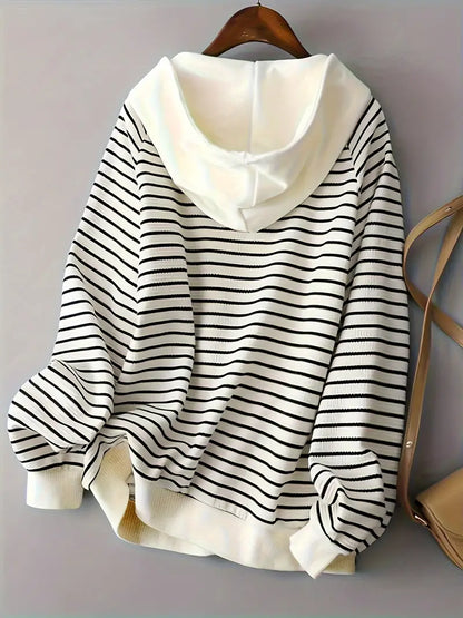 Felpa a righe bianche e nere con cappuccio, appesa su gruccia. Moda casual, abbigliamento donna, stile autunnale.