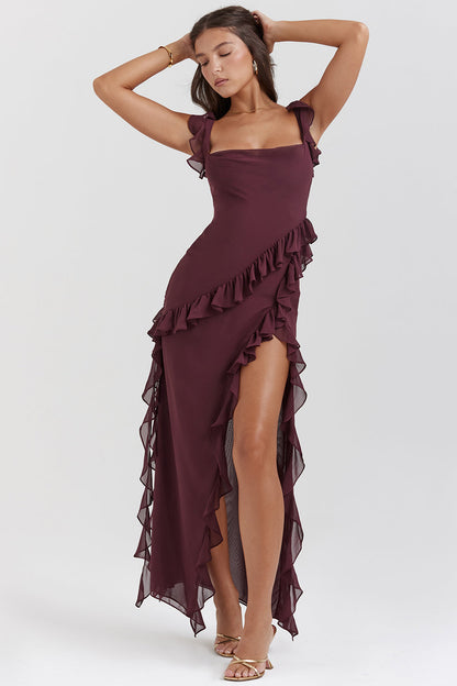 Donna in abito lungo bordeaux con volant, spacco laterale e sandali dorati. Moda elegante, abbigliamento da sera, stile sofisticato.