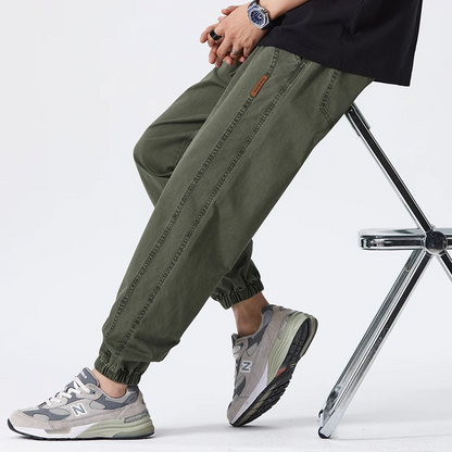 Pantaloni cargo verdi da uomo, stile casual, abbinati a scarpe sportive grigie, seduto su una sedia. Moda streetwear, comfort quotidiano.