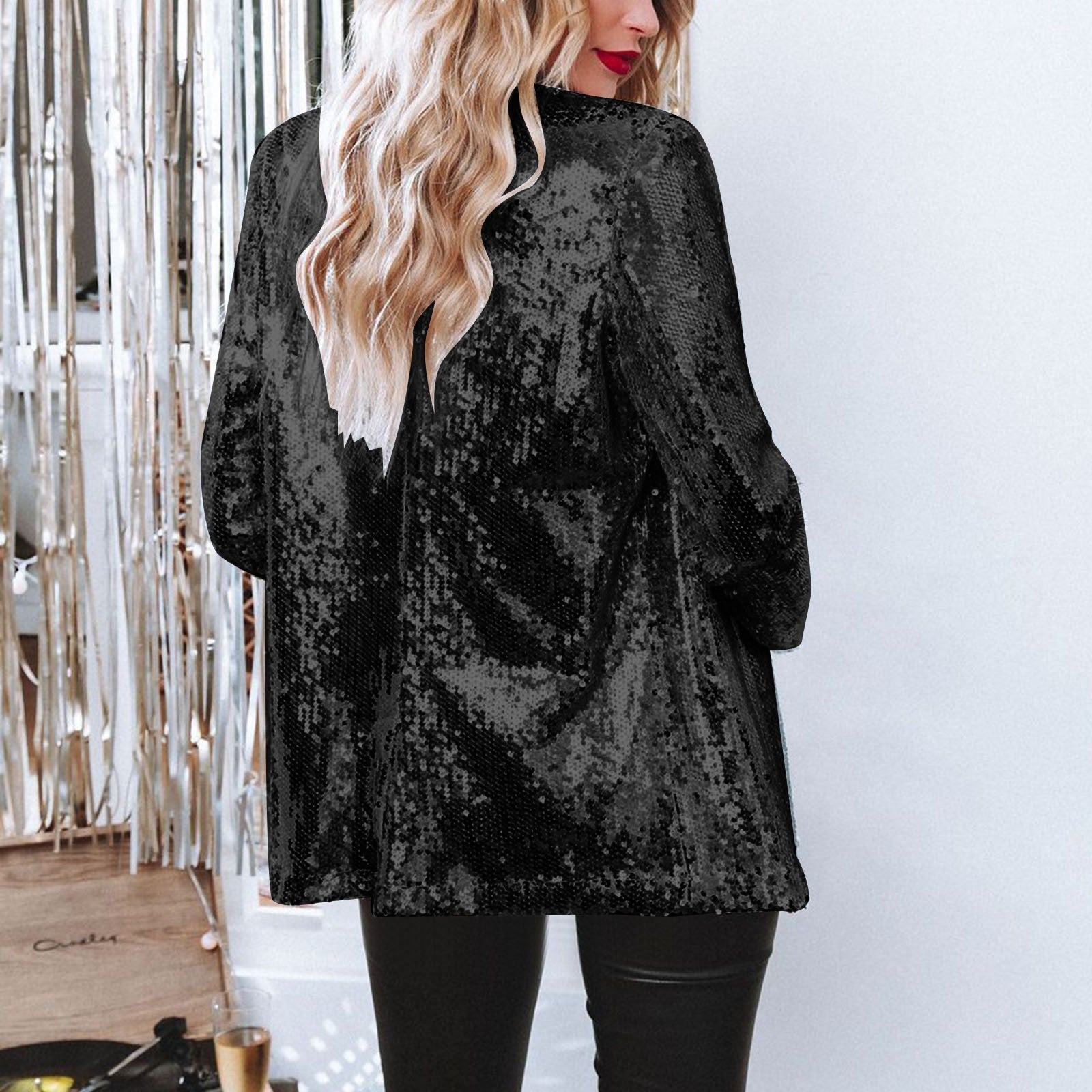 Donna con giacca di paillettes nere, capelli biondi ondulati, in un ambiente elegante. Moda glamour, abbigliamento da sera, stile sofisticato.