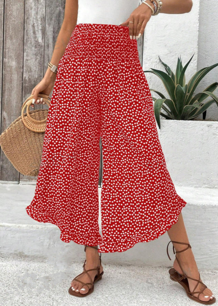 Donna con pantaloni palazzo rossi a pois bianchi, borsa di paglia rotonda, sandali marroni, pianta verde sullo sfondo. Moda estiva casual.
