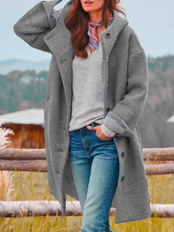 Donna con cappotto grigio oversize, jeans e sciarpa colorata, in un paesaggio autunnale. Moda autunno inverno, abbigliamento casual elegante.