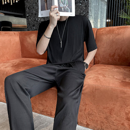 Uomo seduto su divano arancione, indossa abbigliamento nero elegante, tiene una rivista davanti al viso. Interno moderno con dettagli di design.