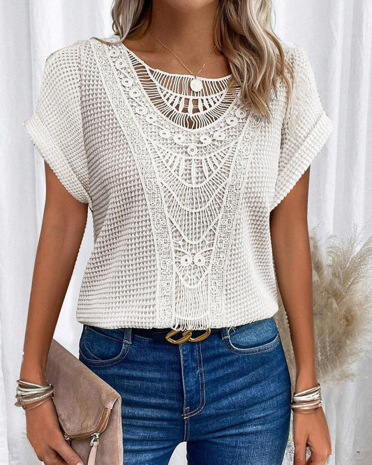 Donna con maglia bianca traforata, jeans blu e accessori argento. Moda estiva elegante, stile casual chic. Clutch beige in mano.