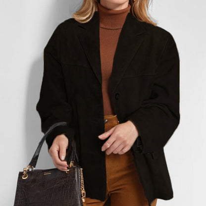 Donna con cappotto nero elegante, maglione marrone e pantaloni color cammello, tiene una borsa in pelle nera. Moda autunnale chic e sofisticata.