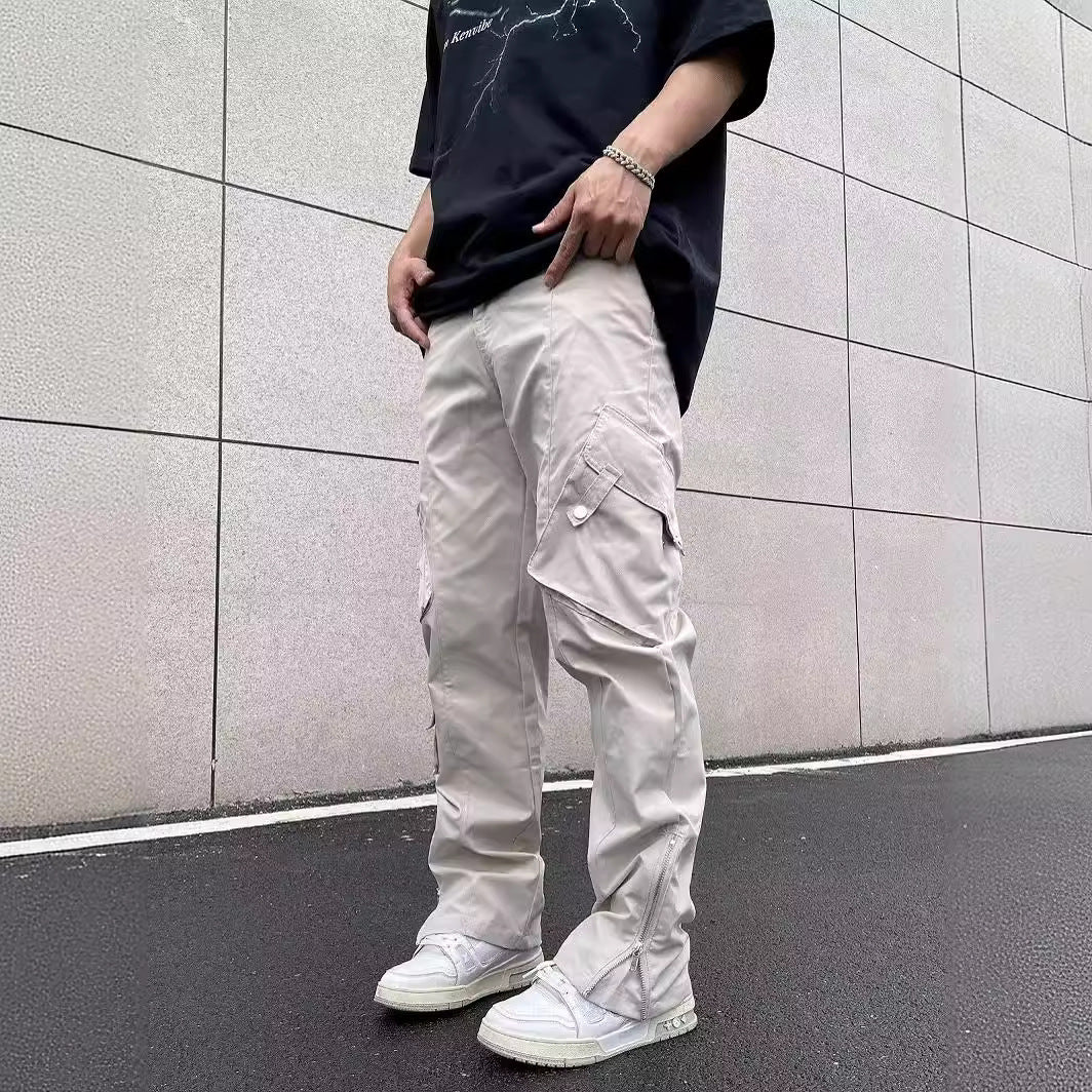 Uomo con pantaloni cargo beige e scarpe da ginnastica bianche su strada asfaltata, indossa maglietta nera. Moda urbana casual, stile streetwear.