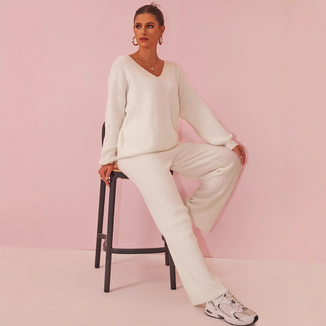 Donna seduta su sedia, indossa completo maglia bianco, scarpe da ginnastica, sfondo rosa. Moda casual elegante, abbigliamento autunnale donna.