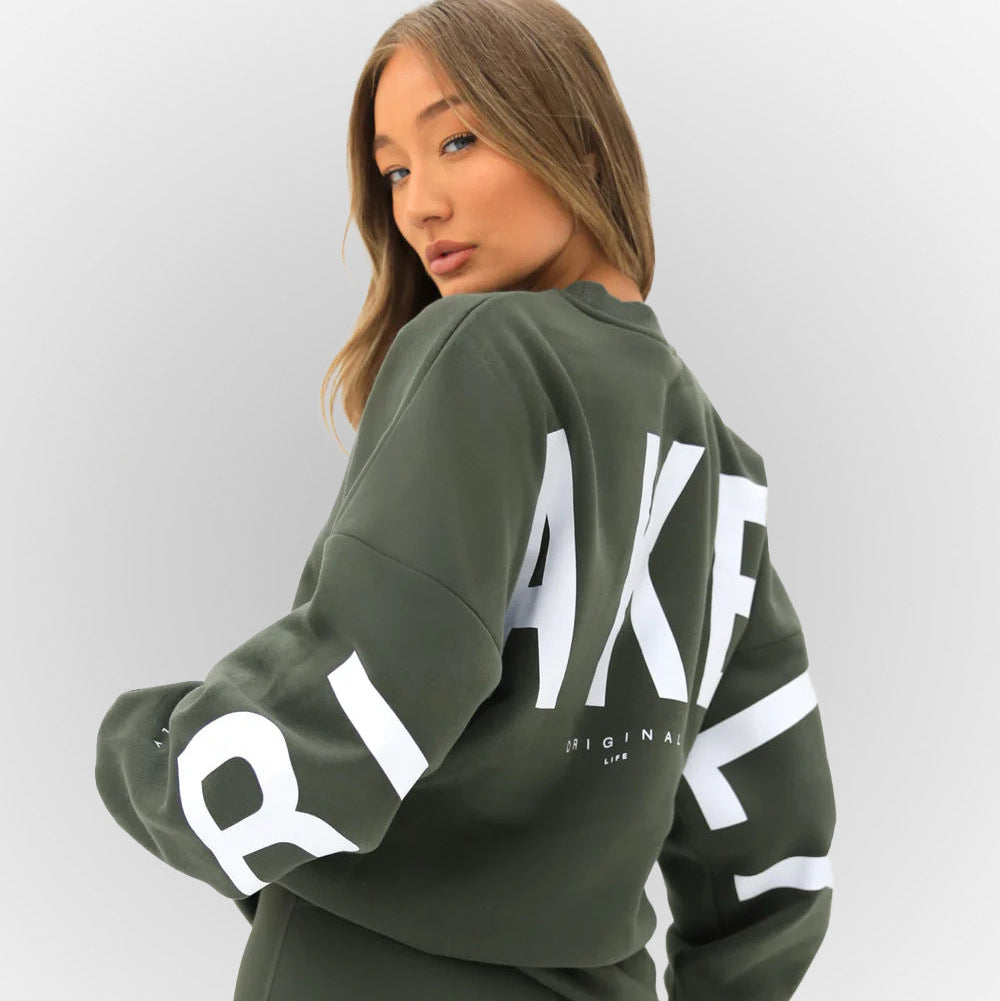 Donna con felpa verde scuro, scritta bianca "AKFL" sul retro. Moda casual, abbigliamento streetwear, stile urbano, tendenze autunno.