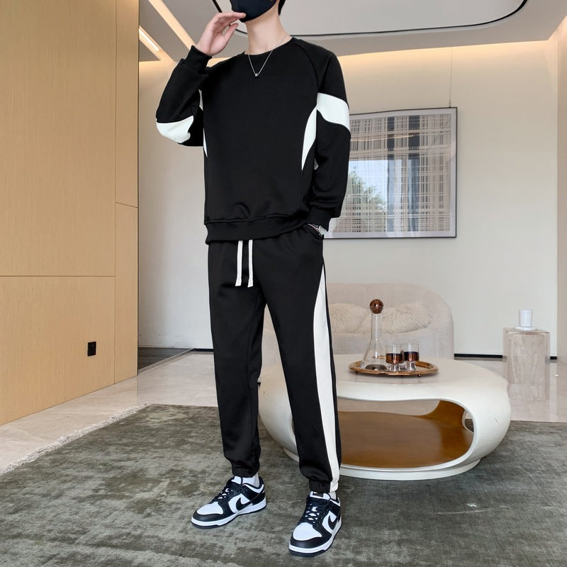 Uomo in tuta sportiva nera con dettagli bianchi, scarpe da ginnastica bianche e nere, in salotto moderno. Stile casual, moda uomo, abbigliamento sportivo.
