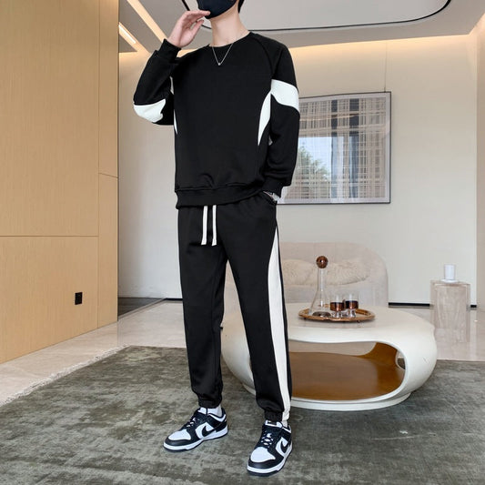 Uomo in tuta sportiva nera con dettagli bianchi, scarpe da ginnastica bianche e nere, in salotto moderno. Stile casual, moda uomo, abbigliamento sportivo.