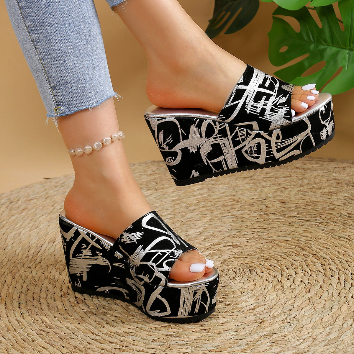 Sandali con zeppa neri e bianchi con design grafico, indossati con jeans chiari. Scarpe estive moda donna, tacco alto, su tappeto intrecciato.