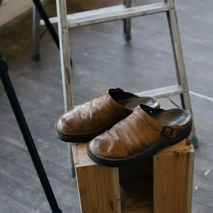 Scarpe di cuoio marrone su blocco di legno, sfondo scala in metallo. Calzature artigianali vintage, moda retrò, design classico.