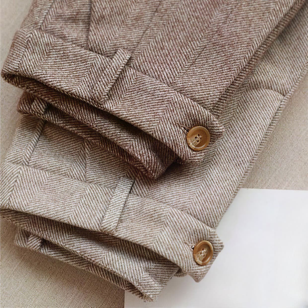 Pantaloni in lana a spina di pesce marrone chiaro, piegati, con bottoni in legno. Tessuto elegante e classico, ideale per moda autunnale.