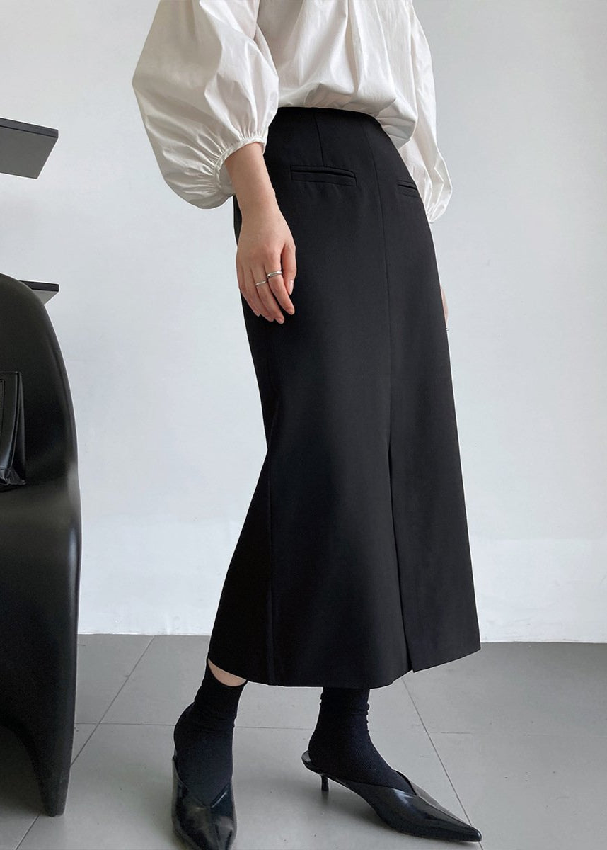 Donna in camicia bianca e gonna nera a vita alta, scarpe nere a punta, posa elegante. Moda minimalista, abbigliamento chic, stile contemporaneo.