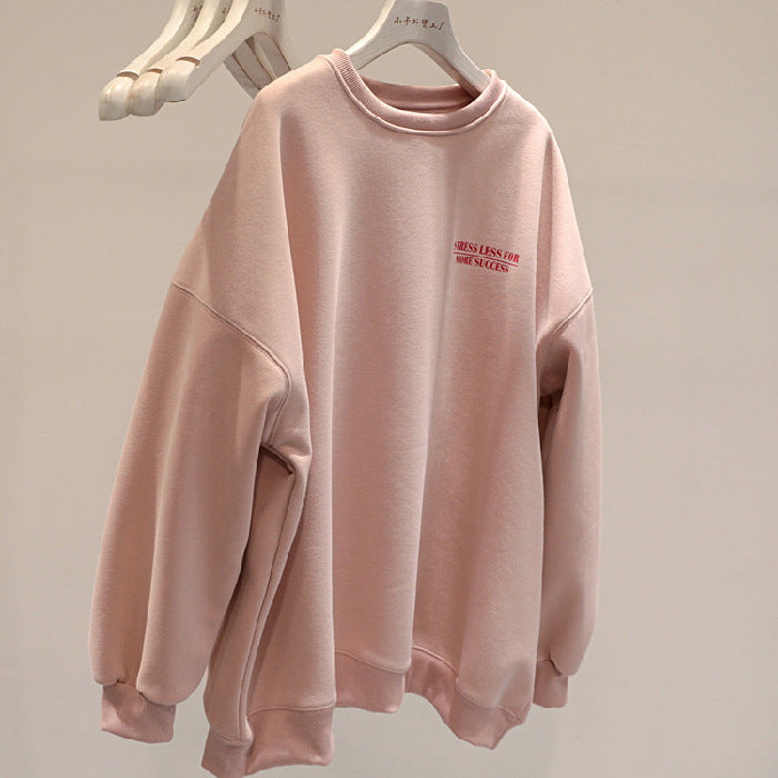 Felpa oversize rosa chiaro con scritta rossa, appesa su gruccia bianca. Moda casual, abbigliamento comodo, tendenza streetwear.