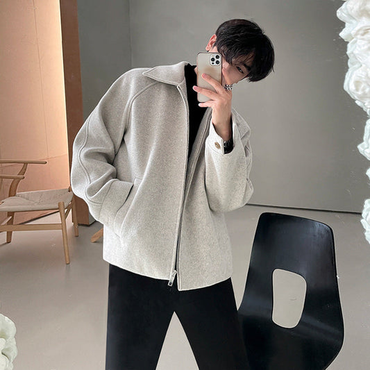 Giovane uomo in giacca grigia elegante, posa davanti a uno specchio con smartphone. Moda autunnale, stile casual, interni moderni.