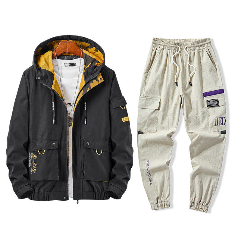Giacca nera con cappuccio giallo e pantaloni cargo beige con tasche multiple. Abbigliamento casual uomo, stile urbano, moda streetwear.