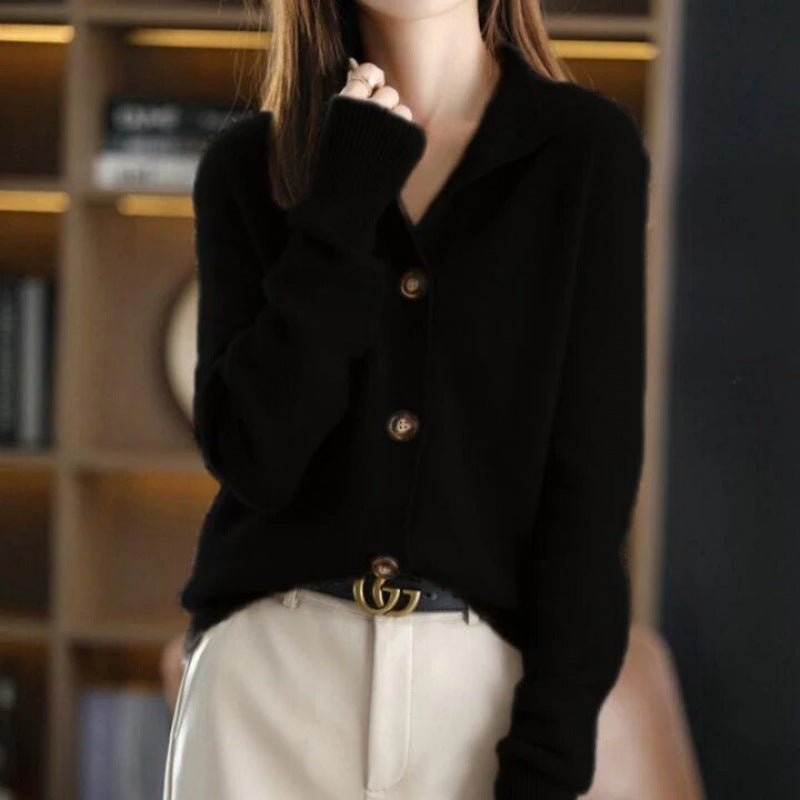Donna con cardigan nero e pantaloni beige, cintura con fibbia dorata, sfondo libreria sfocata. Moda autunno, abbigliamento casual elegante.