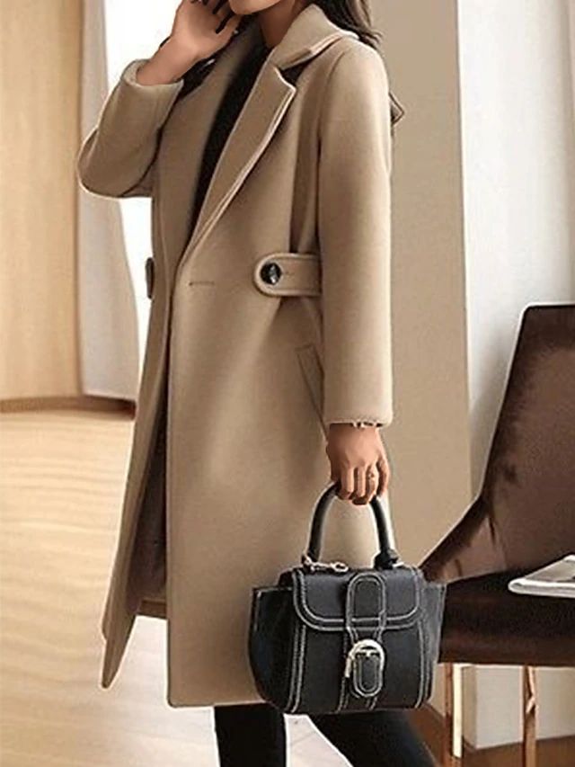 Cappotto beige elegante con cintura, abbinato a borsa nera in pelle con fibbia. Moda autunnale donna, stile sofisticato e moderno.