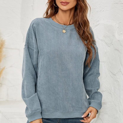 Donna con maglione blu a coste, capelli castani ondulati, collana dorata, sfondo bianco. Moda casual autunnale, abbigliamento femminile trendy.