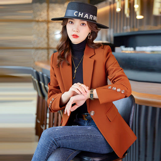 Donna elegante con cappello nero e blazer arancione, seduta in un bar moderno. Moda autunnale, stile sofisticato, abbigliamento casual chic.