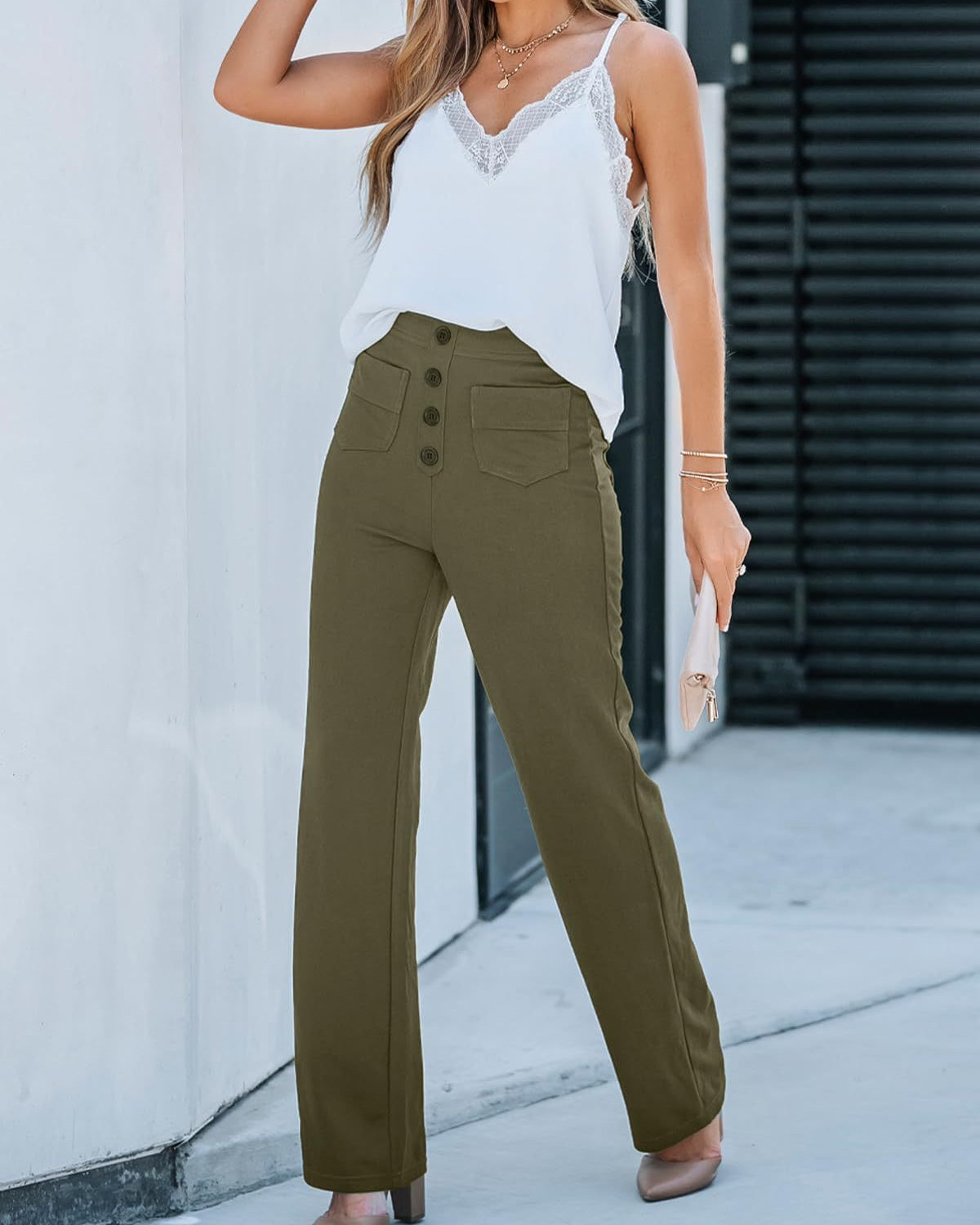 Donna con top bianco in pizzo e pantaloni a vita alta verde oliva, bottoni frontali, posa all'aperto. Moda estiva elegante e casual.