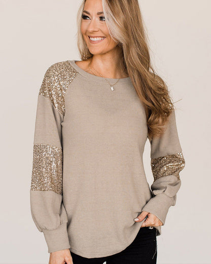 Donna sorridente con maglia beige, maniche lunghe con paillettes dorate. Moda autunnale, abbigliamento casual elegante.