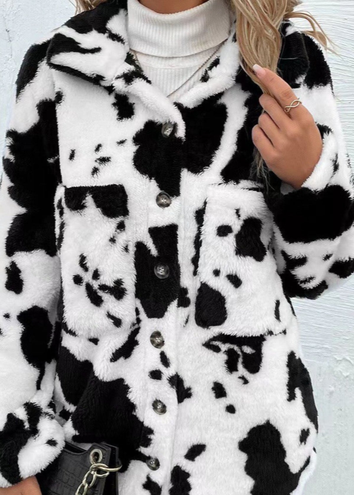 Giacca in pelliccia sintetica bianca e nera con motivo mucca, indossata da una donna con maglione a collo alto bianco. Moda autunno inverno.