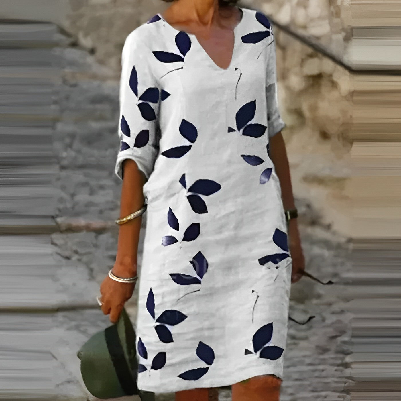 Abito estivo bianco con foglie blu, maniche a tre quarti, scollo a V, indossato da una donna su strada acciottolata. Moda casual elegante.