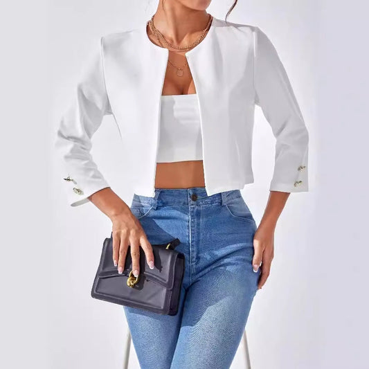 Donna con giacca bianca elegante, top corto e jeans aderenti, tiene una borsa nera. Moda femminile, abbigliamento casual chic, stile moderno.