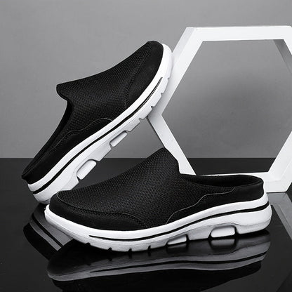 Scarpe slip-on nere da uomo con suola bianca, design sportivo e traspirante, posizionate su sfondo grigio con elemento geometrico bianco.