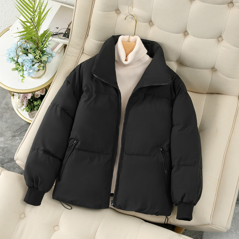 Giacca invernale nera imbottita su sedia beige, con maglione a collo alto crema. Moda invernale, abbigliamento caldo, stile casual elegante.