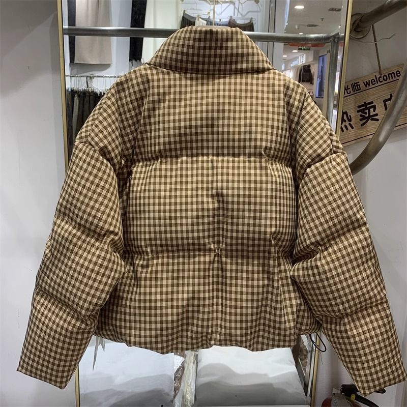 Giacca imbottita a quadri marroni e beige, esposta su appendiabiti in negozio. Moda invernale, abbigliamento caldo, stile casual.