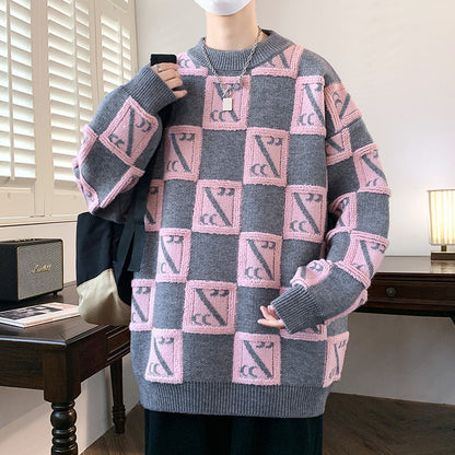 Maglione oversize grigio e rosa con motivo geometrico, indossato da una persona in una stanza moderna. Arredamento minimalista sullo sfondo.