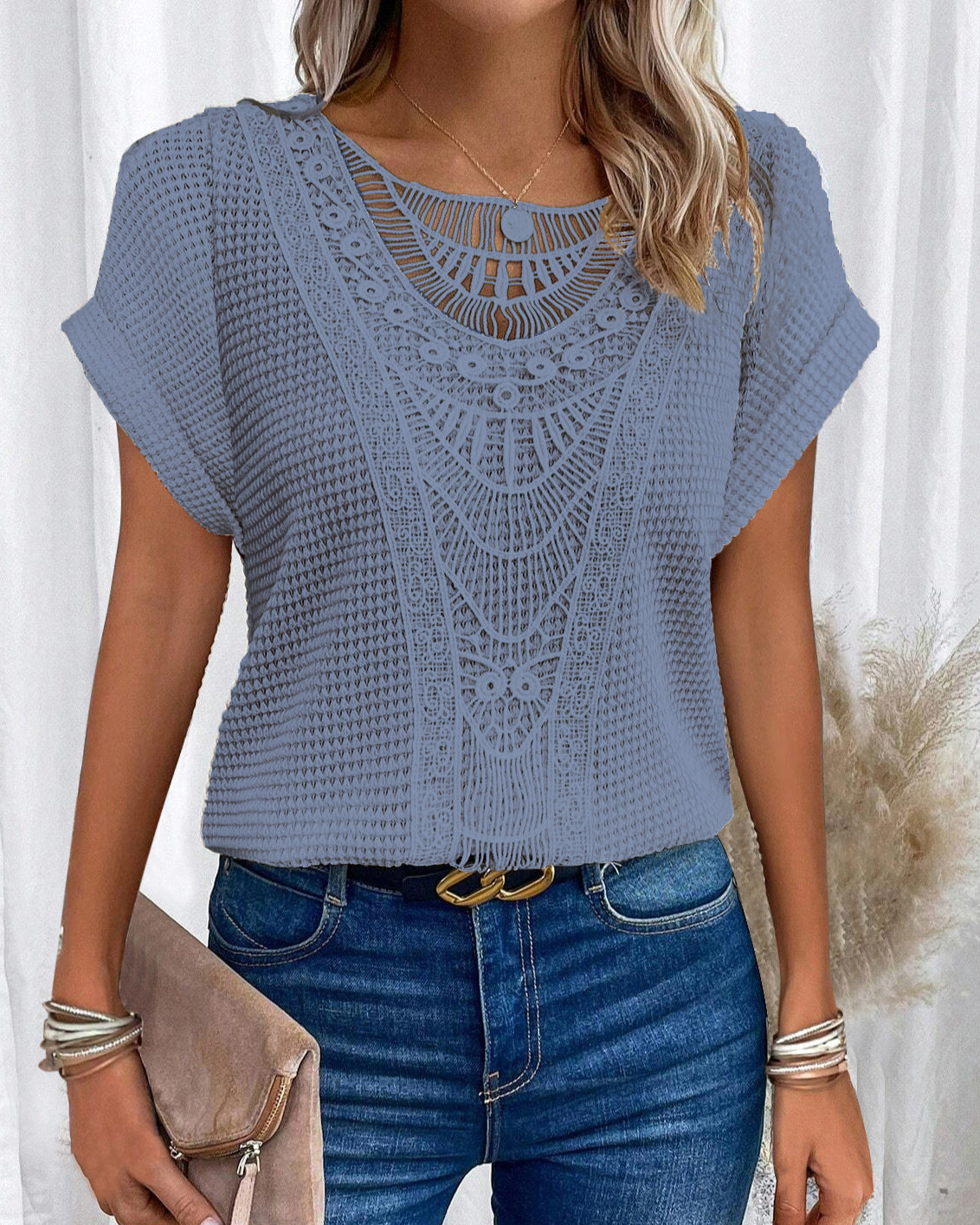 Donna con maglia blu in pizzo crochet, jeans a vita alta, borsa beige e bracciali. Moda estiva casual, abbigliamento femminile trendy.