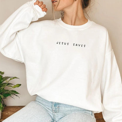 Donna con felpa bianca "Jesus Saves", jeans chiari, posa casual. Moda casual donna, abbigliamento streetwear, stile minimalista.