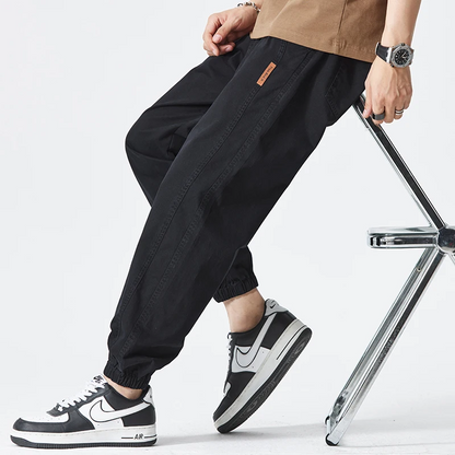 Pantaloni jogger neri da uomo, abbinati a scarpe sportive Nike bianche e nere, su sfondo bianco. Moda casual, abbigliamento streetwear.