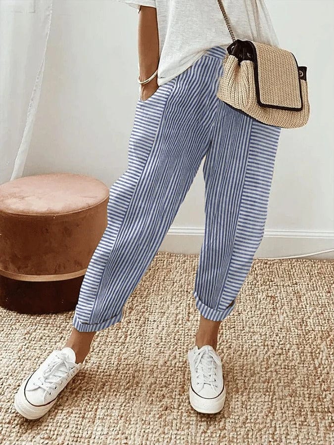 Pantaloni a righe blu e bianche, abbinati a scarpe da ginnastica bianche e borsa di paglia. Look casual estivo per donna.